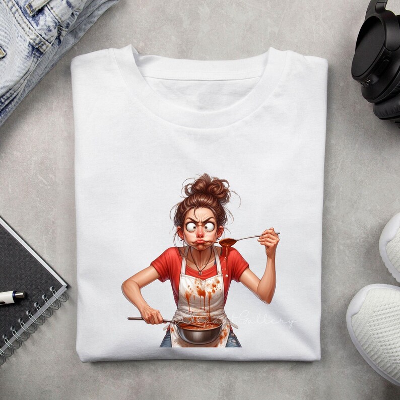 May include: White t-shirt featuring a cartoon illustration of a woman tasting food from a pot. The woman wears a red shirt, a white apron with sauce stains, and has a surprised expression. The image is a humorous depiction of cooking.