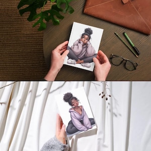 May include: A white journal featuring an illustration of a person in a relaxed pose, wearing a light purple hoodie, gray pants, and white sneakers. The journal is held by hands against a neutral background.