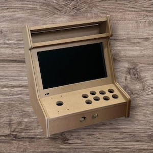 May include: A small, unfinished wooden arcade cabinet with a black screen, eight button holes, and two joystick holes. The cabinet has a rectangular shape with a top shelf and is designed for a retro gaming experience.
