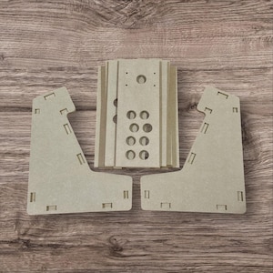 May include: Unassembled light brown wooden arcade game kit. The kit includes side panels, a control panel, and other components with pre-cut holes and slots for assembly. The pieces are arranged on a wooden surface.