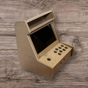 May include: A small, unfinished arcade cabinet made of light brown wood. It features a screen, button holes, and a top shelf. The cabinet is designed to house arcade game components.