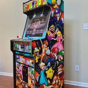 May include: A vertical arcade cabinet featuring a Multicade marquee and a screen displaying a game menu. The side panel is decorated with colorful graphics of various video game characters including Mario, Luigi, Peach, Bowser, and Donkey Kong.