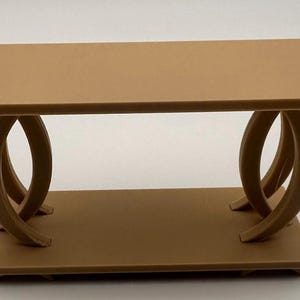 May include: A small, tan table with a rectangular top and a lower shelf. The table's legs have a unique design, featuring curved, oval shapes. The table is approximately 30 cm long, 15 cm wide, and 15 cm tall.