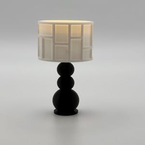 May include: A black table lamp with a white geometric patterned lampshade. The lamp base is made of three stacked spheres.
