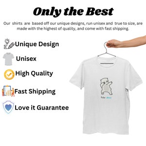 Pode incluir: Uma camiseta branca com um urso polar de desenho animado dan&ccedil;ando na frente. O texto "Polar Brrr" est&aacute; impresso abaixo do urso. A camiseta est&aacute; pendurada em um cabide.