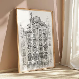May include: A framed black and white architectural sketch of a building with ornate details, including arched windows and a decorative rooftop. The artwork is displayed in a gold-colored frame, leaning against a wall.