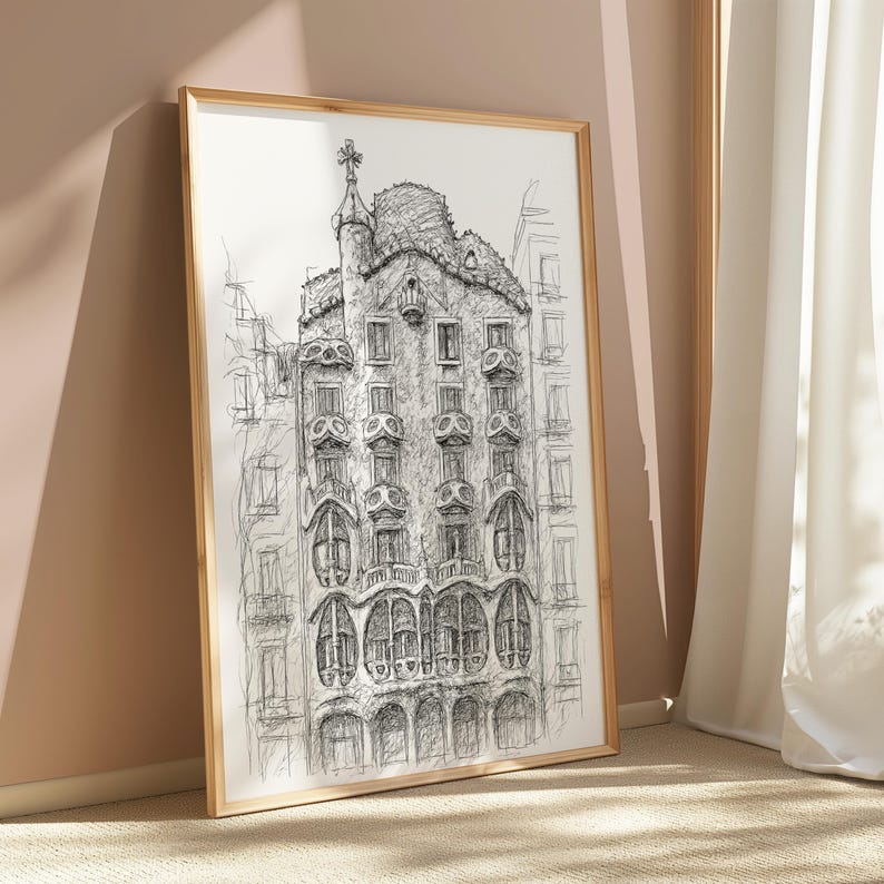 May include: A framed black and white architectural sketch of a building with ornate details, including arched windows and a decorative rooftop. The artwork is displayed in a gold-colored frame, leaning against a wall.