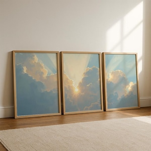 May include: Three framed art prints showing a sky scene with clouds and sunlight. The artwork uses blues, whites, and yellows, with the sun's rays shining through the clouds. The frames are light wood, and the prints are leaning against a white wall.