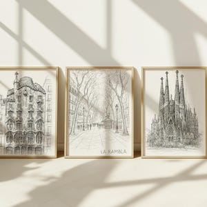 May include: Three framed black and white architectural sketches. The sketches depict a building with ornate details, a tree-lined street with the text "LA RAMBLA", and a cathedral with tall spires. The frames are a light wood color.