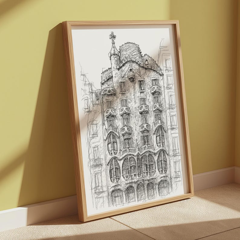 May include: A framed black and white architectural sketch of a building with ornate details, including arched windows and a decorative tower. The artwork is displayed in a light-colored wooden frame, leaning against a yellow wall.