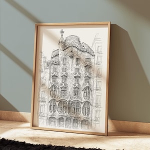 May include: A framed black and white architectural sketch of a building with ornate details, including arched windows and a decorative rooftop. The artwork is displayed in a light-colored wooden frame, leaning against a wall.