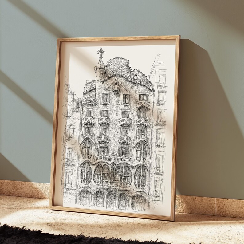 May include: A framed black and white architectural sketch of a building with ornate details, including arched windows and a decorative rooftop. The artwork is displayed in a light-colored wooden frame, leaning against a wall.