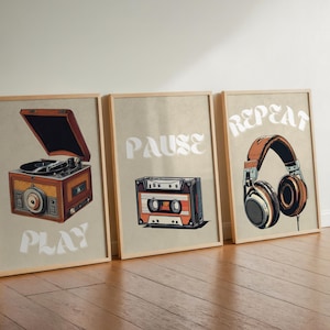 Può includere: Tre stampe incorniciate con apparecchiature musicali vintage e le parole "Play", "Pause" e "Repeat". La stampa a sinistra presenta un giradischi vintage, la stampa al centro presenta un nastro per cassette e la stampa a destra presenta un paio di cuffie.