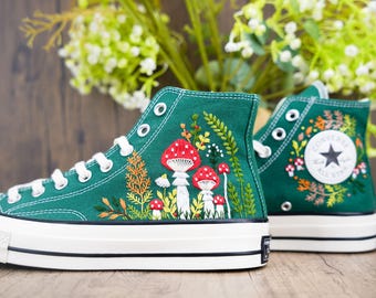 May include: Green high-top canvas sneakers with white stitching and a white rubber sole. The sneakers are embroidered with a floral design and red and white mushrooms.