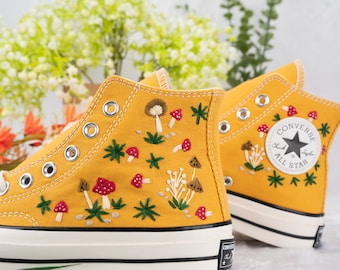 Puede incluir: Zapatillas Converse de caña alta amarillas con champiñones, hojas y estrellas bordadas. El logotipo de Converse All Star es visible en el lateral de la zapatilla.