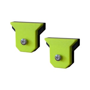May include: Two T-shaped brackets featuring a bright lime green textured front panel attached to a black base. Each bracket is secured with a single silver-colored metal hex bolt centered on the front face, showcasing a functional design.