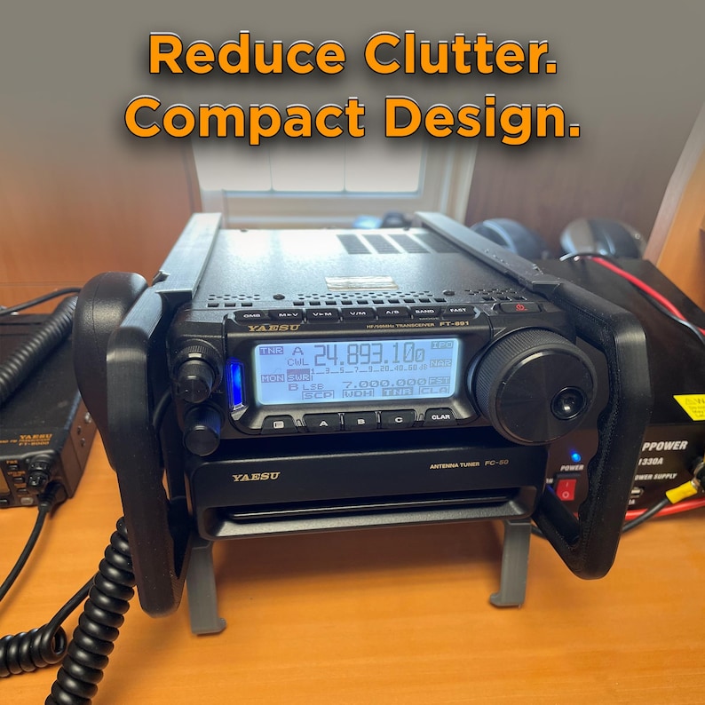 May include: A black Yaesu FT-891 HF/VHF transceiver and FC-50 antenna tuner mounted in a black metal stand. The transceiver features a digital display showing 24.893.10 and the text Reduce Clutter. Compact Design. is visible above the unit.