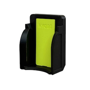 May include: Black plastic power tool holder with a neon green insert. The word "RYOBI" is printed on the green insert. The holder has a curved base and two curved side supports.