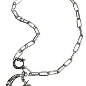 May include: Silver-toned chain necklace with a crescent moon and star pendant. The moon has an openwork design, and the star is a five-pointed shape. The necklace has a lobster clasp closure.