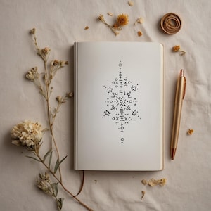 Può includere: Un quaderno bianco con un disegno geometrico nero disegnato sulla pagina. Il quaderno è appoggiato su una superficie di tessuto bianco con fiori secchi e una penna dorata.