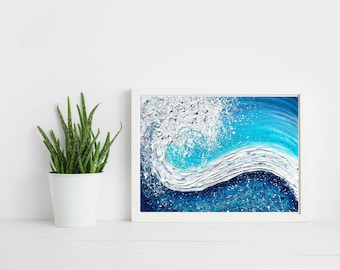 Op de afbeelding: Een ingelijst abstract schilderij van een blauwe golf die breekt met wit schuim. Het schilderij is in een wit frame en staat op een wit oppervlak.