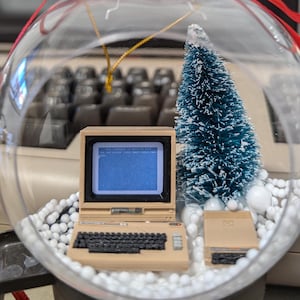 Könnte beinhalten: Ein transparenter Weihnachtsbaumschmuck aus Glas mit einem Miniatur-Beige-Computer, einem kleinen blauen Tannenbaum und weißem Styropor-Schnee. Der Computerbildschirm zeigt den Text "YOU ARE IN TROUBLE! CALL NOW! PRESS F1!"