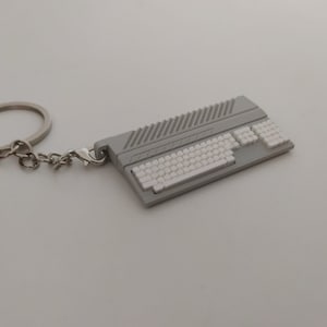 Könnte beinhalten: Ein grauer und weißer Computer-Tastatur-Schlüsselanhänger mit einem silbernen Schlüsselring und einer Kette.