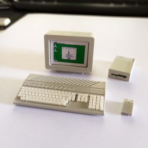 Puede incluir: Un conjunto de ordenador blanco en miniatura con un monitor, un teclado y dos componentes adicionales. El monitor muestra una pantalla verde con texto.