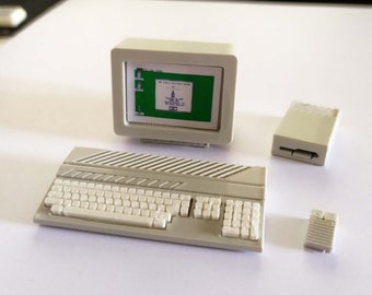 Puede incluir: Un conjunto de ordenador blanco en miniatura con un monitor, un teclado y dos componentes adicionales. El monitor muestra una pantalla verde con texto.