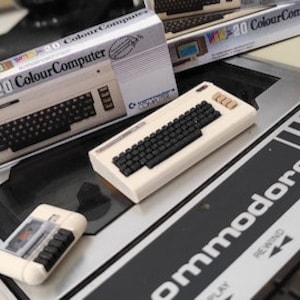 May include: A miniature replica of a vintage Commodore 20 Colour Computer, complete with a keyboard, cassette drive, and box packaging. The computer is beige with black keys and a black cassette drive.