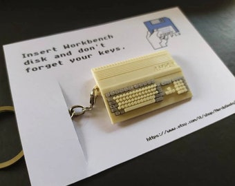 May include: A white keychain shaped like a vintage computer with a keyboard and the text "Insert Workbench disk and don't forget your keys." The keychain is attached to a silver key ring.