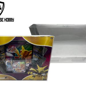 Puede incluir: Una vitrina de plástico transparente con un sobre de juego de cartas coleccionables Pokémon con Alakazam V. El sobre tiene un diseño morado, dorado y amarillo con imágenes de Alakazam y otros Pokémon.