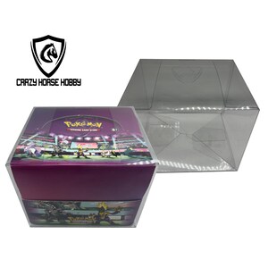 Può includere: Una scatola di plastica trasparente con all'interno una scatola di booster del Gioco di Carte Collezionabili Pokémon di colore viola e bianco. La scatola presenta il logo "Gioco di Carte Collezionabili Pokémon" e una classificazione di età 6+. La scatola è su una superficie bianca.