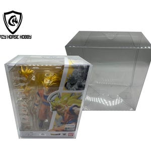 Puede incluir: Una vitrina de plástico transparente con una figura de anime amarilla y naranja en su interior. La figura es de un personaje con el pelo de punta y un atuendo amarillo y naranja. La vitrina está etiquetada con "S.H.Figuarts" y "Dragon Ball Super".