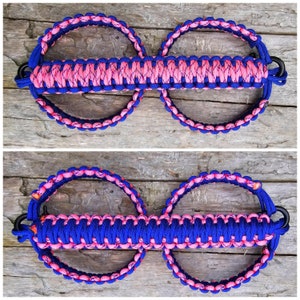 May include: A pair of blue and pink paracord loops with black metal clasps. The loops are connected by a braided strap.