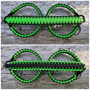 May include: A black and green paracord double loop handle. The handle is made of two loops connected by a braided section. The loops are black with green edging, and the braided section is green with black edging.