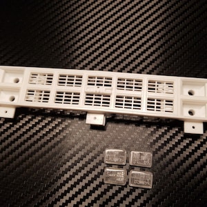 Peut inclure: Grille de voiture modèle en plastique blanc avec un motif en nid d'abeille noir. Quatre petites pièces en métal argenté sont incluses.