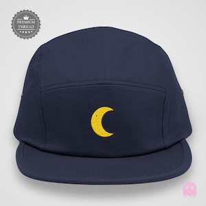 Op de afbeelding: Marineblauwe vijf-panel cap met een gele halve maan geborduurd op de voorkant. De cap heeft een platte klep en een gestructureerd ontwerp. Gemaakt van duurzame stof, met een premium draadlabel.