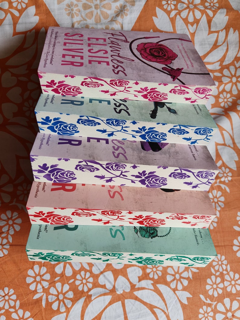 May include: A stack of six paperback books with floral designs on the spines. The titles of the books are "Flawless", "Elsie", "Silver", "Flawless", "Elsie", and "Silver".