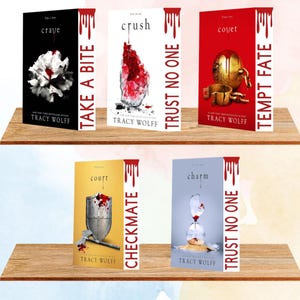 Puede incluir: Exhibición de seis libros de Tracy Wolff, con portadas de varios colores. Los títulos incluyen "Crave", "Crush", "Covet", "Court" y "Charm". Cada libro tiene un diseño único, con texto en los lomos y portadas. Los libros están colocados en una estantería de madera.