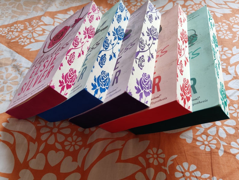 May include: Five paperback books with floral designs and the title "Kiss Ever After" on the spines. The books are stacked on top of each other and have different coloured spines: red, blue, purple, red, and green.