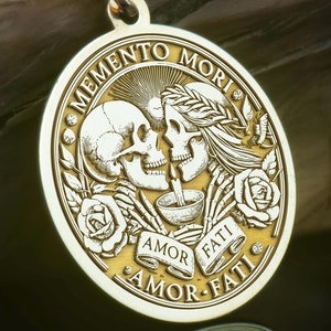 Può includere: Una collana con un ciondolo rotondo in oro inciso che raffigura due scheletri che si abbracciano. Il medaglione ha l'iscrizione "Memento Mori Amor Fati" attorno al bordo.