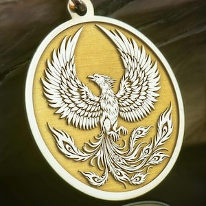 May include: Gold pendant necklace with a phoenix design. The circular pendant features a detailed relief of a phoenix with outstretched wings and tail feathers. The pendant hangs from a fine gold chain. The phoenix is a symbol of rebirth.