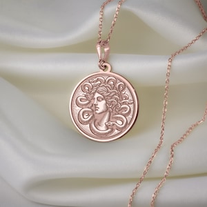 May include: A rose gold necklace with a round pendant featuring a detailed engraving of Medusa's head surrounded by snakes.