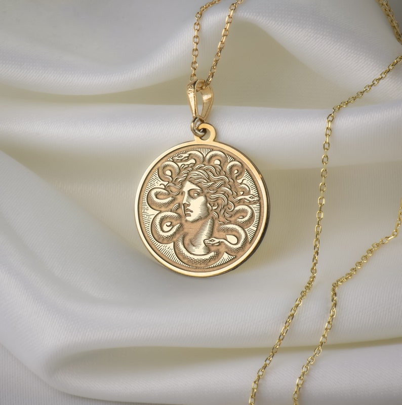 May include: A gold necklace with a round pendant featuring a detailed engraving of Medusa, the Greek mythological figure with snakes for hair.