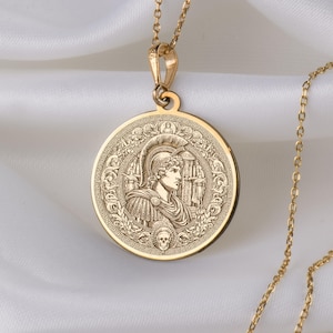 Könnte beinhalten: Eine goldene Kettenkette mit einem runden Anhänger, der ein eingraviertes Bild eines Kriegers in einem Helm zeigt. Der Anhänger hat ein detailliertes Design mit einem Totenkopf am Boden.