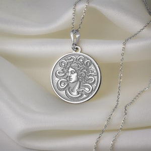 May include: Silver necklace with a round pendant featuring a detailed engraving of Medusa's head surrounded by snakes.