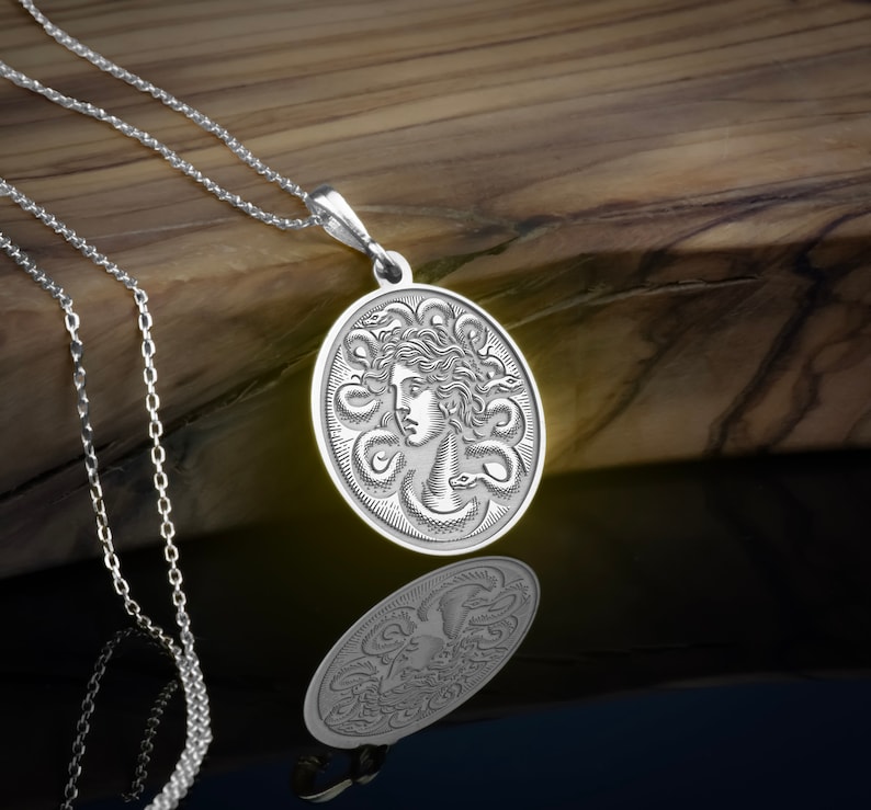 May include: A silver necklace with a round pendant featuring a detailed engraving of Medusa's face surrounded by snakes.