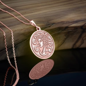 May include: A rose gold necklace with a round pendant featuring a detailed engraving of Medusa's head surrounded by snakes.