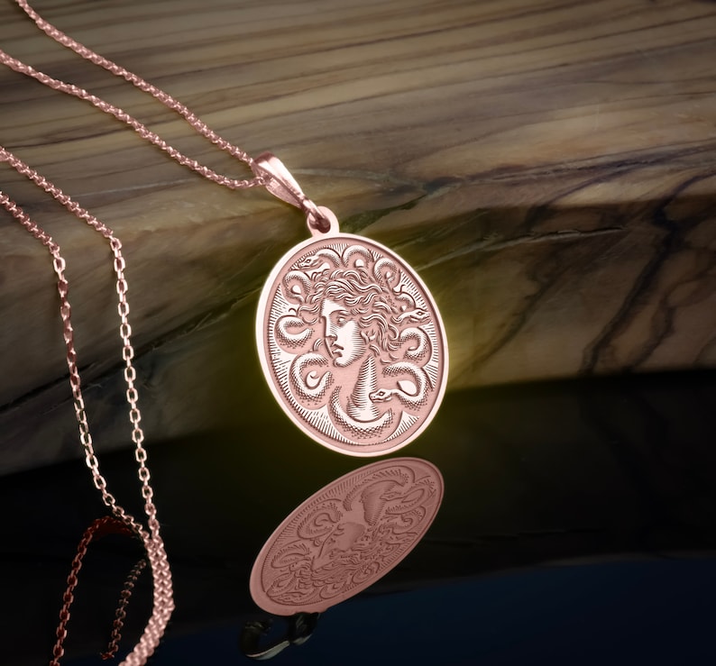 May include: A rose gold necklace with a round pendant featuring a detailed engraving of Medusa's head surrounded by snakes.